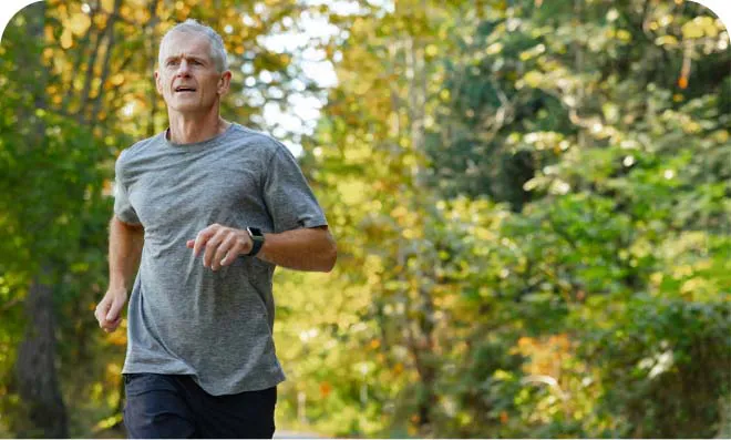 Uomo di circa 60 anni che corre in un bosco
